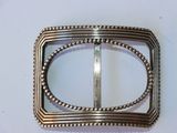 pair of silver metal buckles with beaded edges on a white surface