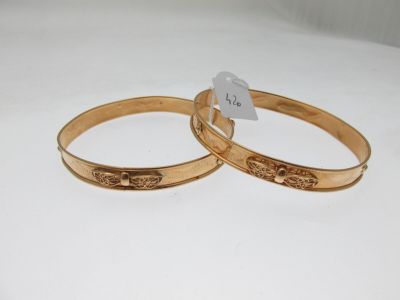 two gold tone bang bracelets with engraved designs on them