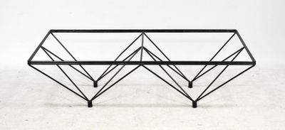 une table basse en métal noir et en verre posée sur un sol blanc