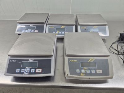 quatre balances électroniques posées sur un plan de travail en métal