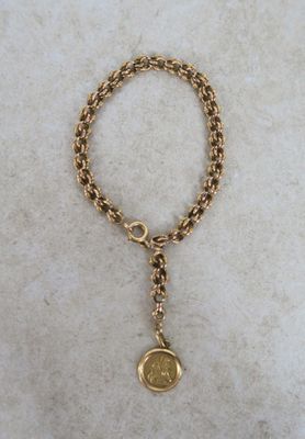 a close up of a gold chain bracelet with a coin on it