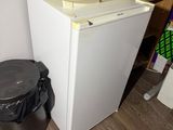 a small white refrigerator next to a trash can