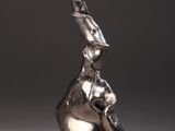 sculpture en argent représentant une femme assise sur un rocher, les mains levées