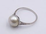 a close up of a white pearl ring on a white surface