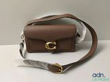 un petit sac à main marron orné d'une boucle dorée, posé sur une table blanche