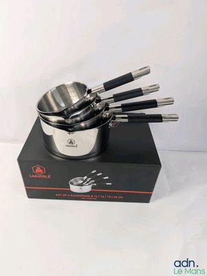 un ensemble de cinq casseroles et poêles en acier inoxydable présenté dans un coffret noir