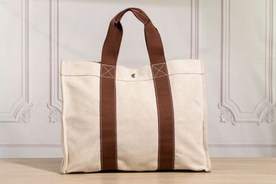 a white canvas tote bag with brown leather handles on a wooden floor