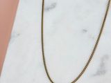 un collier à chaîne en or posé sur une surface en marbre