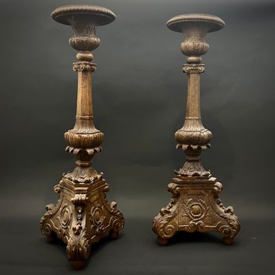 une paire de bougeoirs anciens en bois sculpté sur socles, sur fond sombre