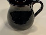 un pichet noir posé sur une table blanche, avec un couvercle marron