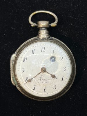 a silver pocket watch with a white face on a black surface