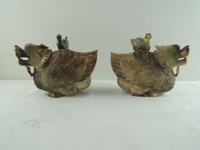 une paire de figurines anciennes en céramique représentant des coqs, posées sur une table blanche