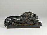 a black sculpture of a lion laying down on a wooden base