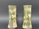pair of green vases with trees on them sitting on a table