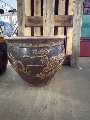 un grand vase marron posé par terre à côté d'une chaise en bois