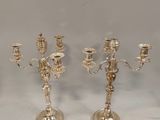 trois chandeliers en argent posés sur une table, sur fond blanc