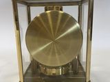 a gold clock in a glass case on a white surface