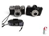 two cameras sitting next to each other on a white surface