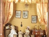 deux poupées dans une vitrine avec des rideaux et des tableaux accrochés au mur