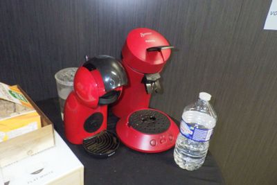 une cafetière rouge posée sur une table à côté d'une bouteille d'eau