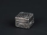a silver box with a design on it sitting on a black surface