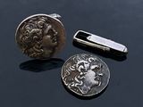a silver coin and a silver tie bar on a black surface