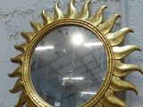 un miroir doré en forme de soleil posé sur une étagère en bois