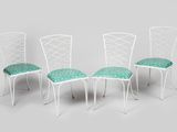 quatre chaises en métal blanc, ornées de coussins verts, sur fond gris