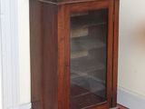 une petite armoire en bois avec une porte vitrée, dans un coin