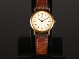 a gold wrist watch with a brown leather band and roman numerals