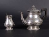 a silver tea pot and a silver cup on a table