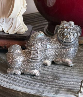 two silver figurines sitting on a table next to a red vase