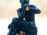 statue of a man sitting on a rock with a gold coin in his mouth
