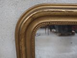 a gold framed mirror hanging on a wall next to a chair