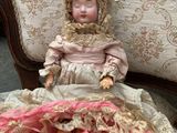 a doll that is sitting on a bed with a pink blanket