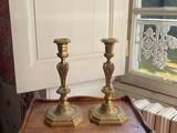 two gold candles on a wooden table near a window