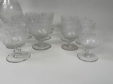 six clear glass goblets and a pitcher sitting on a table