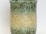 a green and yellow vase sitting on a white surface