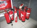 several fire extinguisors are lined up against a brick wall