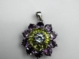a close up of a green and purple flower pendant on a white surface