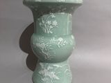 a green vase with white flowers on it sitting on a table