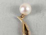 a close up of a pearl and gold pendant on a white surface