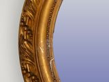 a gold oval mirror hanging on the wall