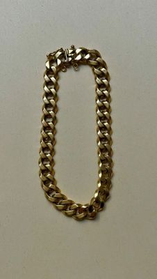 gros plan d'un bracelet en chaîne en or sur une surface blanche