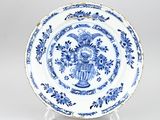 une assiette bleue et blanche sur laquelle est représenté un vase de fleurs