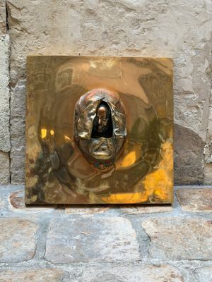 une plaque en or sur laquelle est représenté un visage, posée sur un sol en pierre