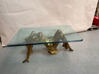 une table en verre sur laquelle est posée une statue en bronze représentant une femme allongée