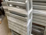 a stack of white wooden chairs in a warehouse
