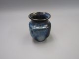 un petit vase bleu posé sur une surface blanche