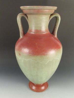 un vase orange et vert posé sur une table blanche